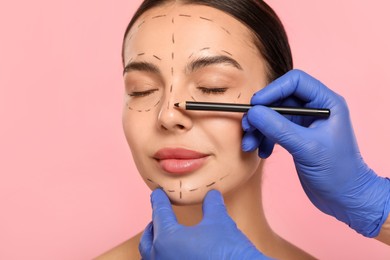 Photo of Doctor with pencil preparing patient for cosmetic surgery operation on pink background, closeup