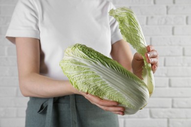 Photo of Woman separating leaf from fresh Chinese cabbage near white brick wall, closeup