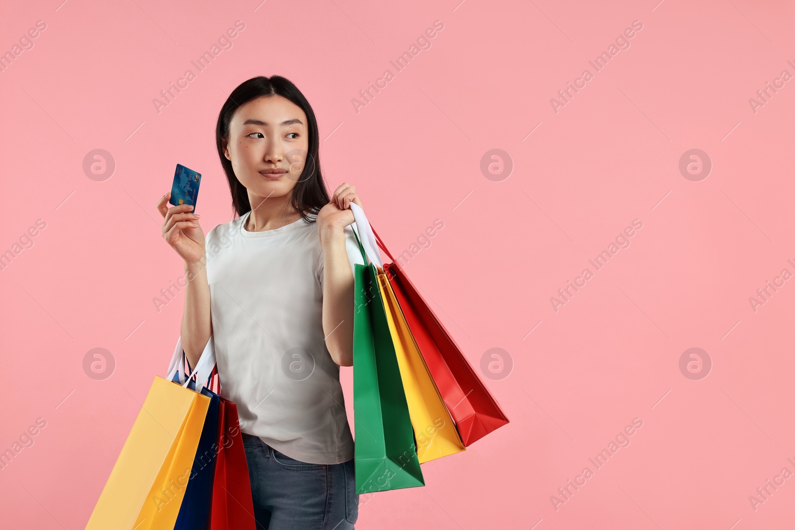 Photo of Beautiful woman with shopping bags and credit card on pink background. Space for text