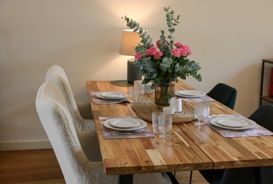 Beautiful table setting with bouquet and candles indoors. Roses and eucalyptus branches in vase