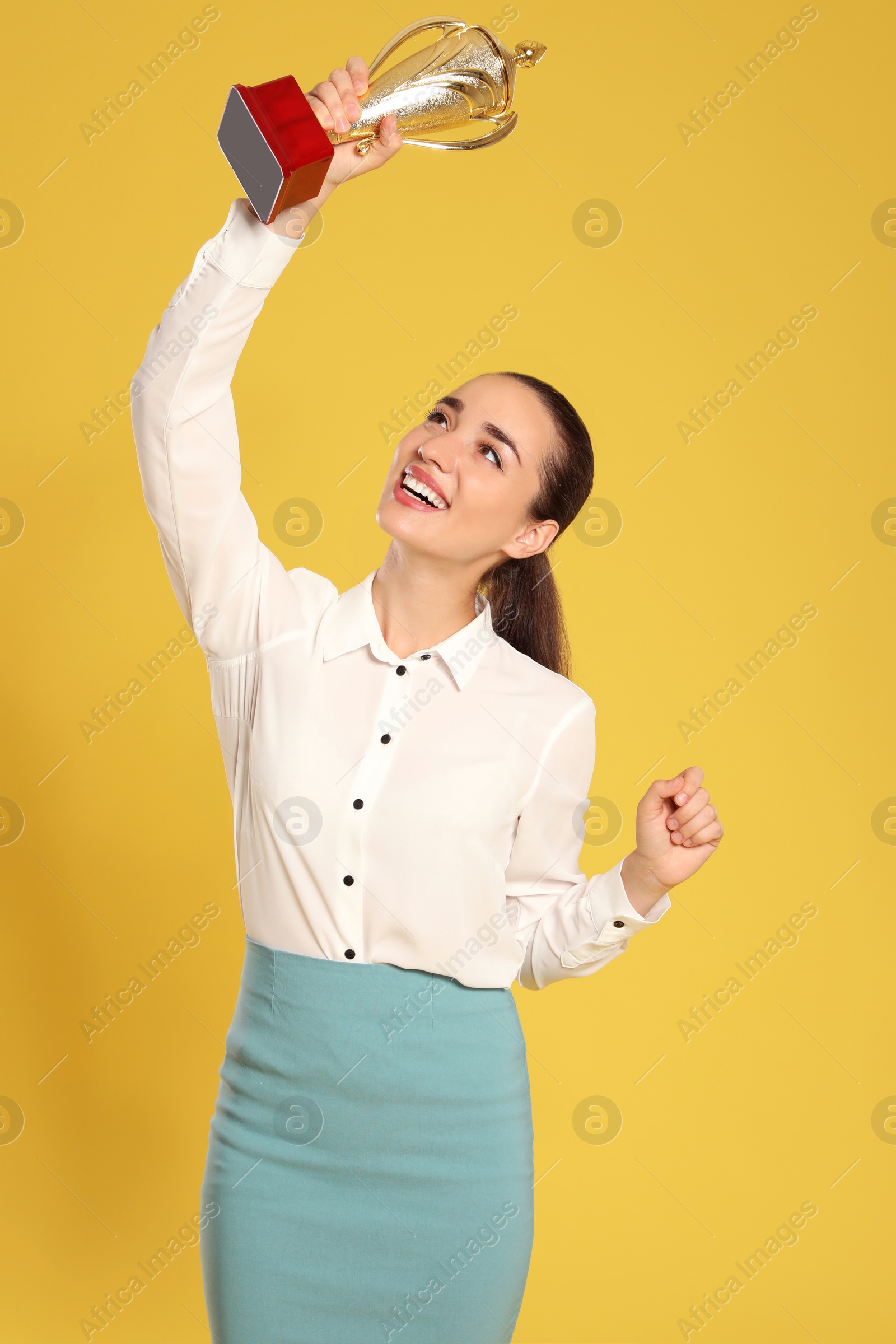 Photo of Portrait of happy young businesswoman with gold trophy cup on yellow background