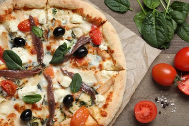 Tasty pizza with anchovies and ingredients on wooden table, flat lay