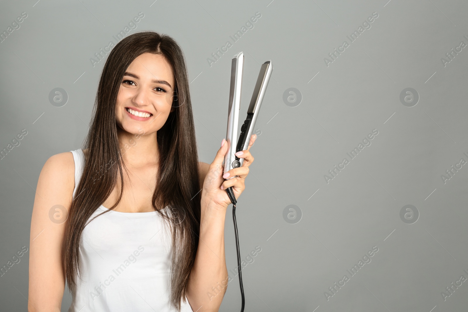 Photo of Young woman with modern hair iron on grey background, space for text