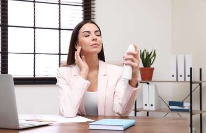 Photo of Young woman applying thermal water on face in office. Cosmetic product