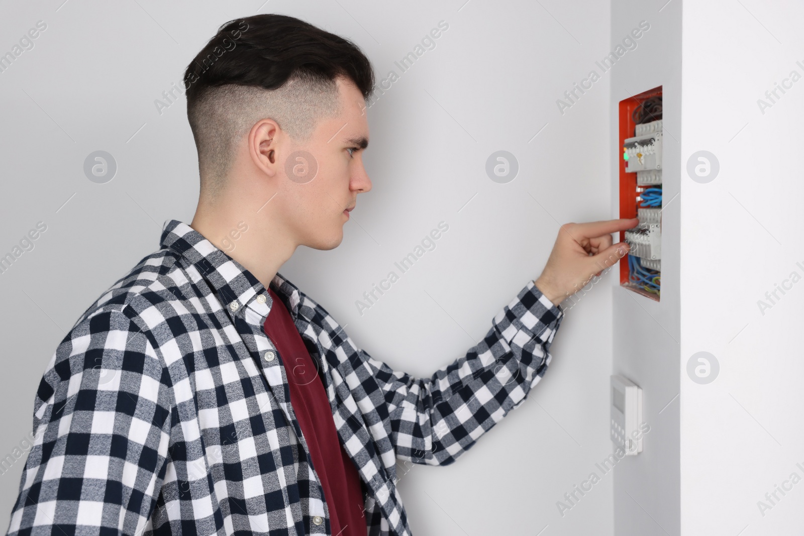 Photo of Young handyman pressing switch on electrical panel board indoors