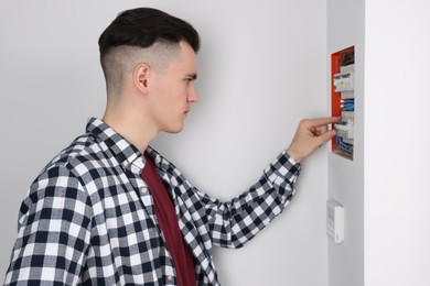 Photo of Young handyman pressing switch on electrical panel board indoors