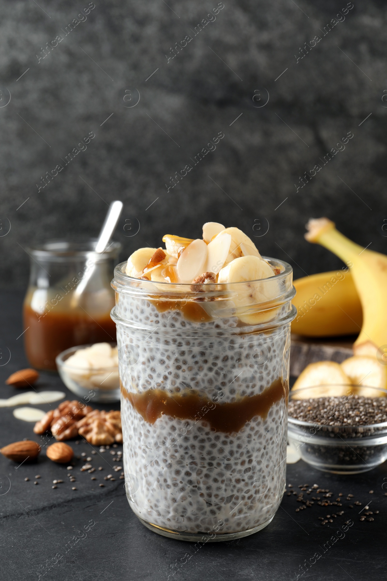 Photo of Delicious chia pudding with banana, walnuts and caramel sauce on black table
