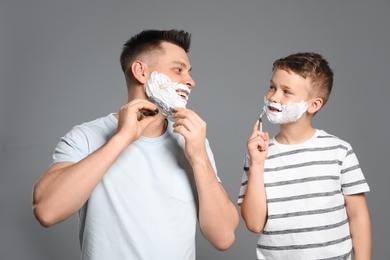 Dad shaving and son imitating him on grey background