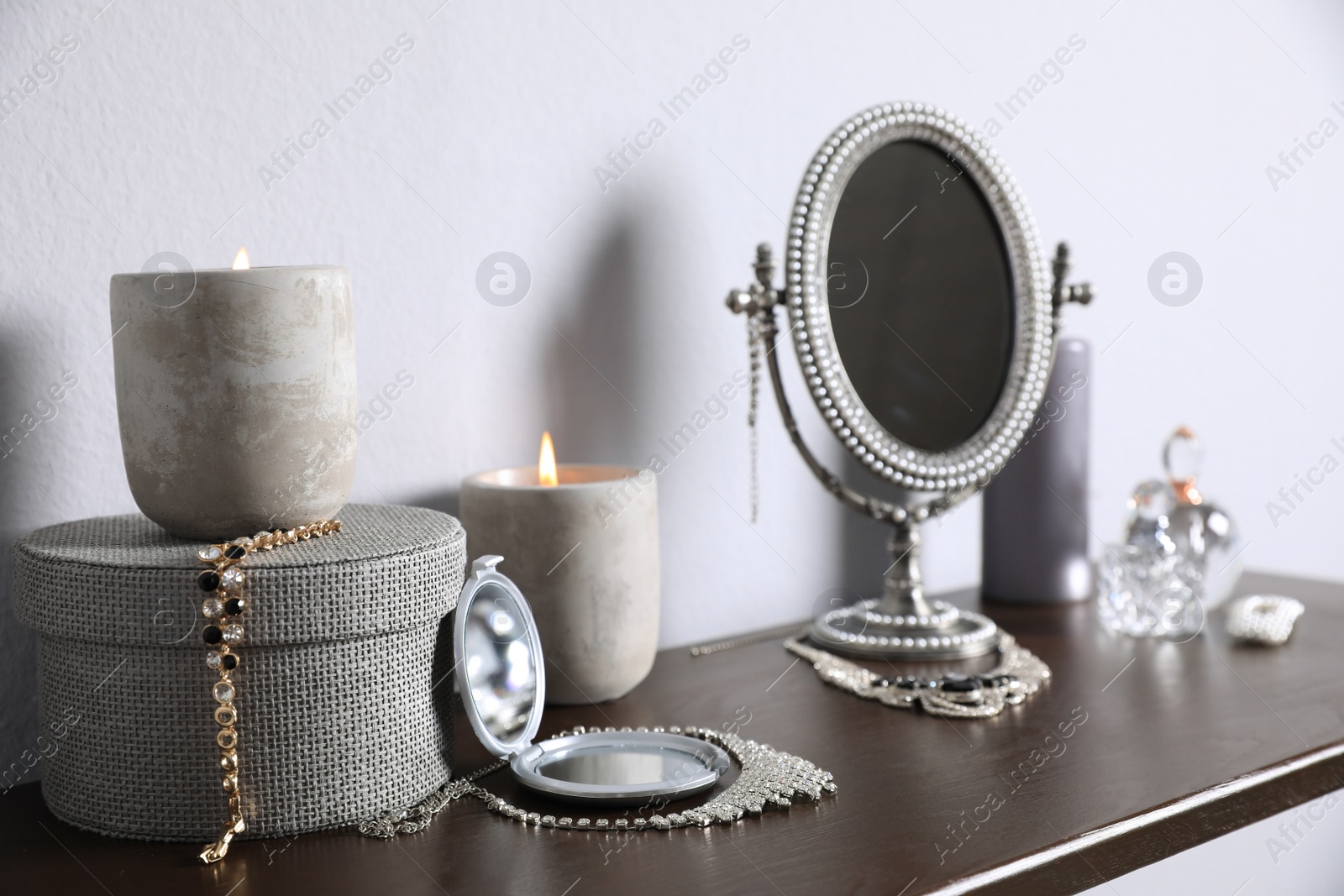 Photo of Small mirror, perfume bottles and jewelry on wooden table near light wall