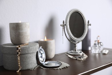 Small mirror, perfume bottles and jewelry on wooden table near light wall