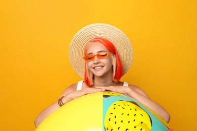 Photo of Beautiful young woman with bright dyed hair and inflatable ball on orange background