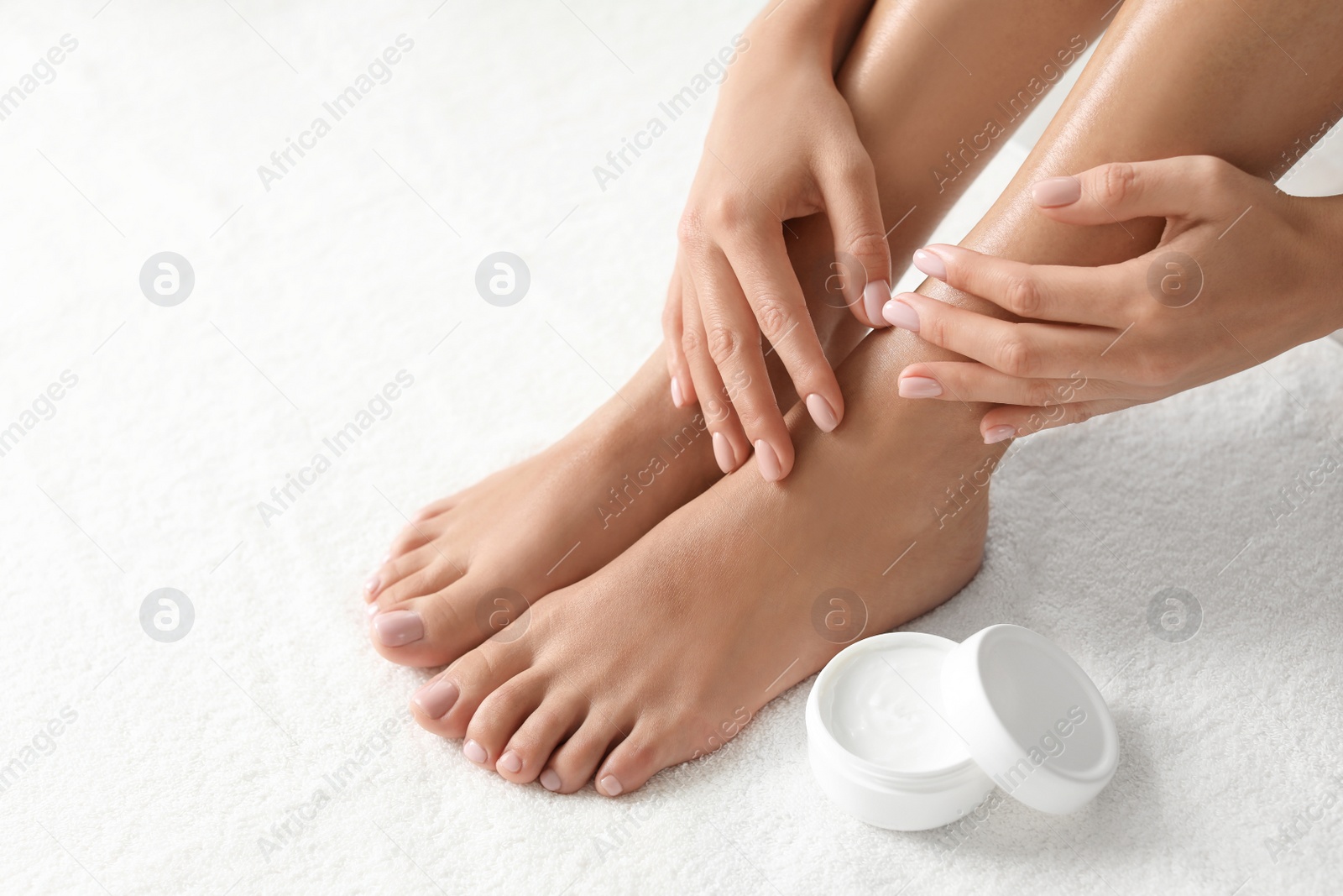 Photo of Woman with beautiful feet and moisturizing cream on white towel, closeup. Spa treatment