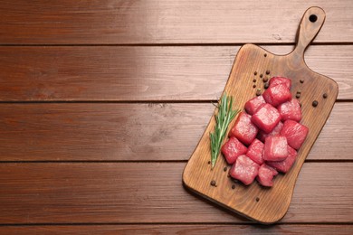 Photo of Cooking delicious goulash. Raw beef meat and rosemary on wooden table, top view with space for text