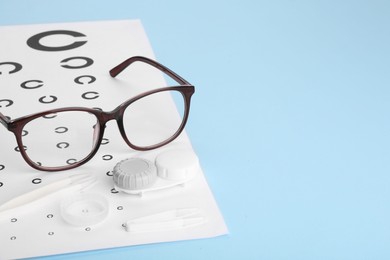 Photo of Vision test chart, glasses, lenses and tweezers on light blue background, space for text