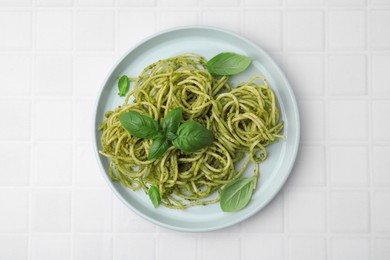 Photo of Delicious pasta with pesto sauce and basil on white tiled table, top view