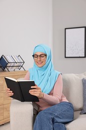 Muslim woman reading book on couch in room