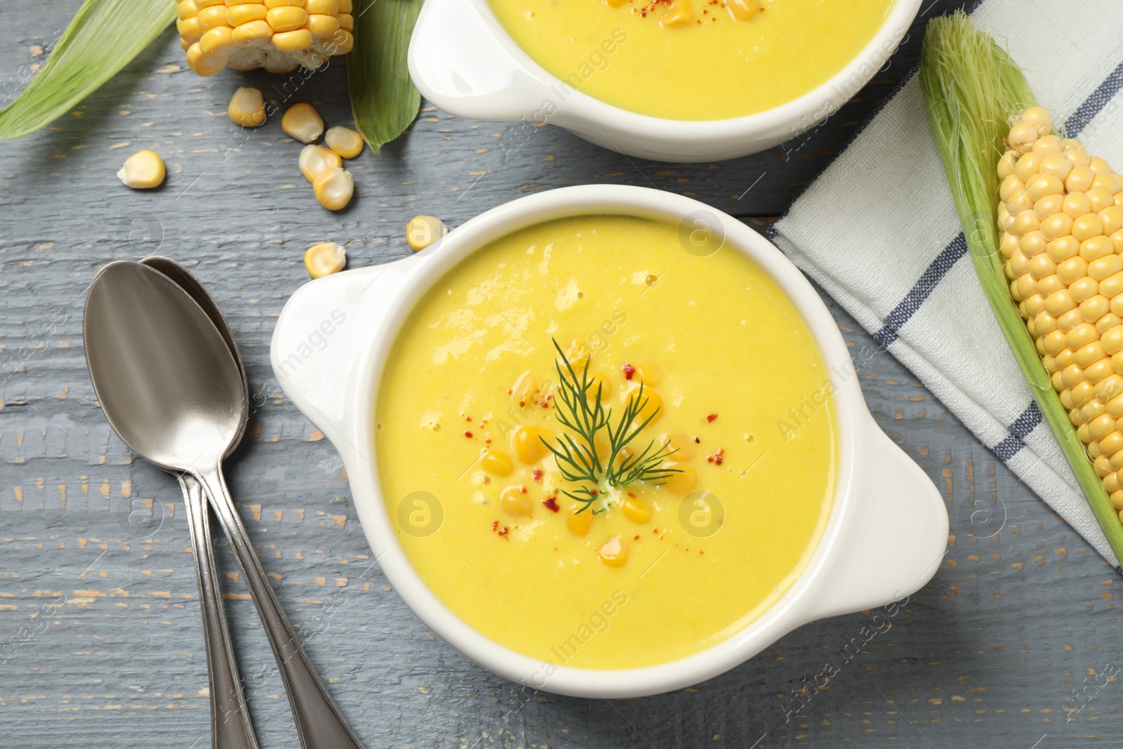 Photo of Delicious creamy corn soup served on grey wooden table, flat lay