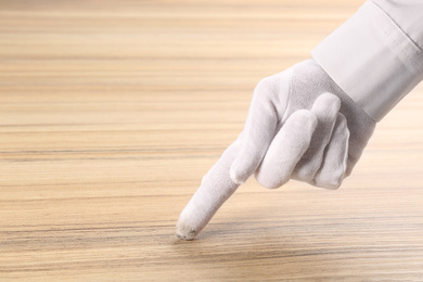 Photo of Person in white glove checking cleanliness of wooden  table, closeup