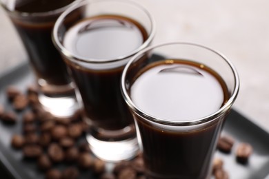 Photo of Shot glasses with coffee liqueur and beans on table, closeup