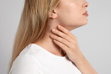 Photo of Young woman doing thyroid self examination on light grey background, closeup