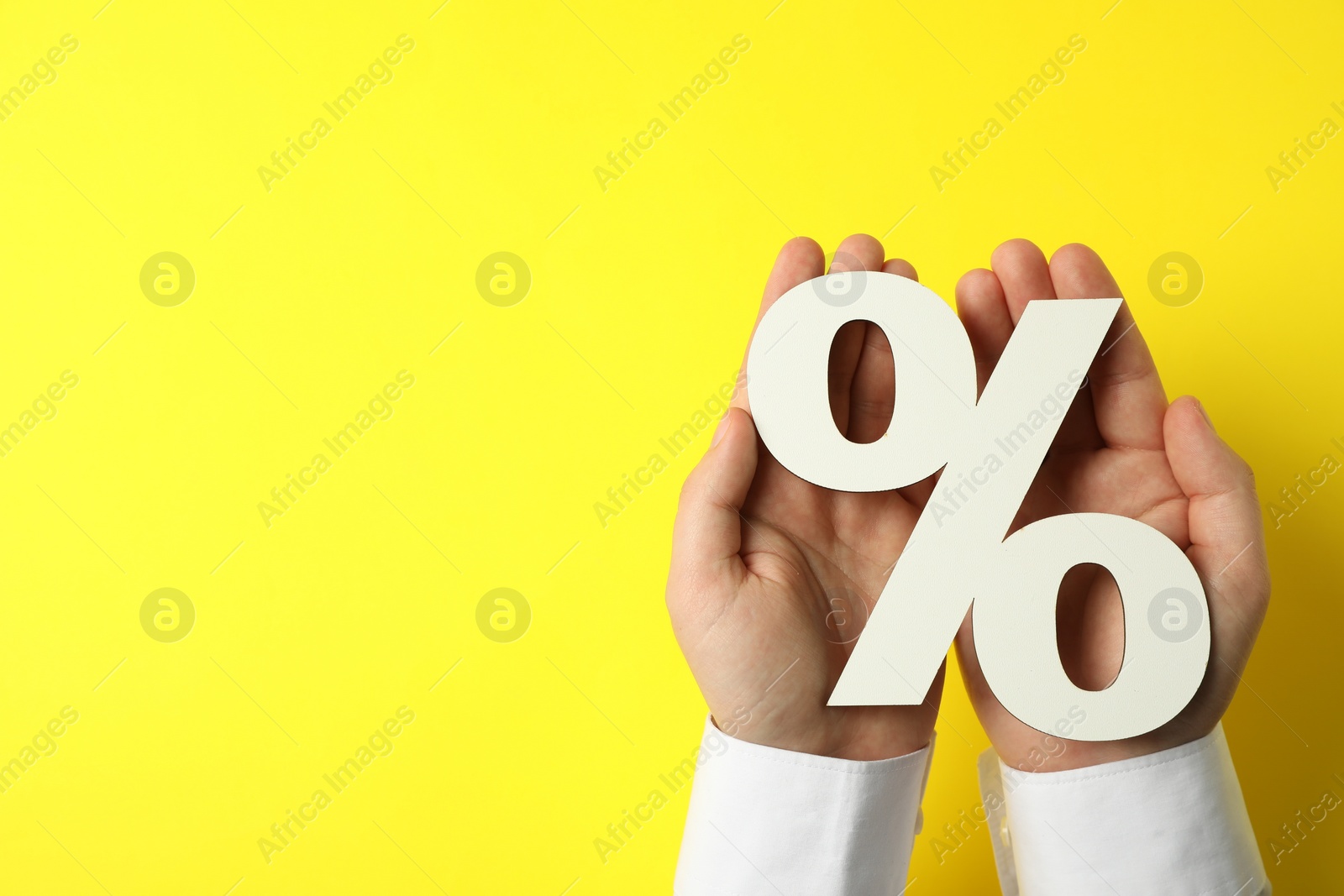 Photo of Man holding percent sign on yellow background, top view. Space for text