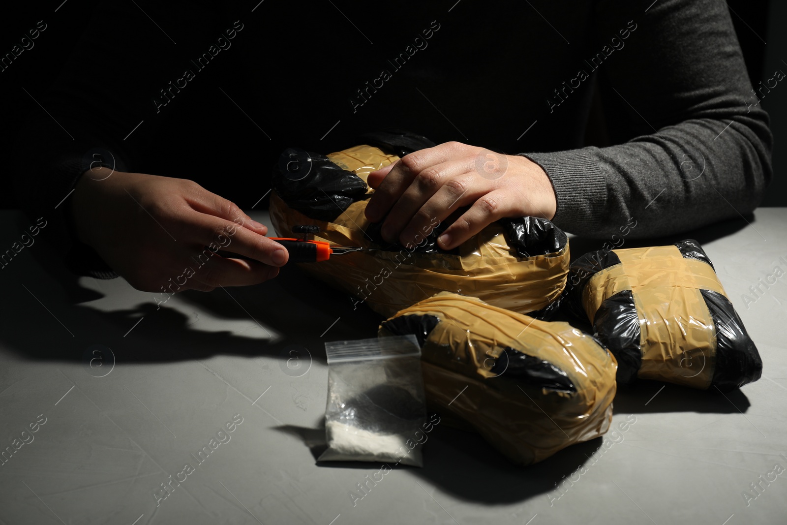 Photo of Smuggling and drug trafficking. Man opening package of narcotics with box cutter in darkness, closeup