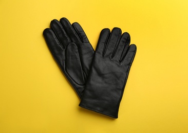 Photo of Pair of stylish leather gloves on yellow background, flat lay