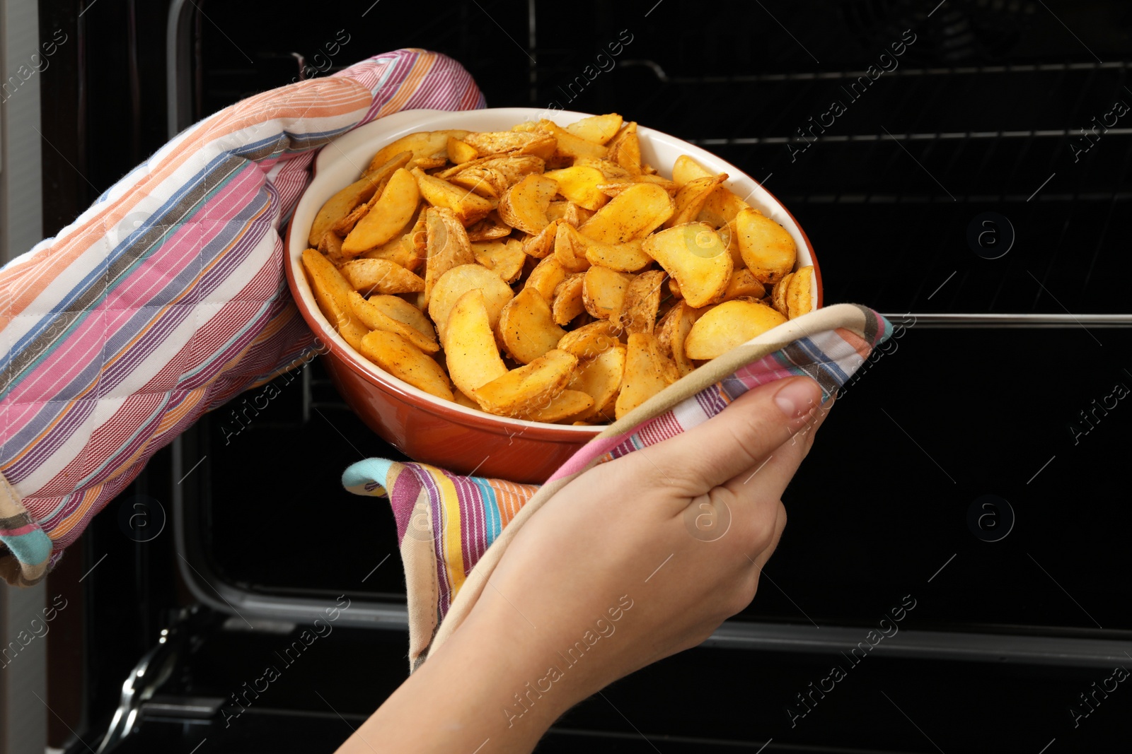 Photo of Woman taking hot roasted potatoes out of oven, closeup