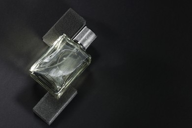 Stylish presentation of luxury men`s perfume in bottle on black background, top view. Space for text