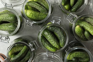 Pickling jars with fresh cucumbers on grey table, flat lay