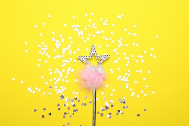 Photo of Beautiful silver magic wand with feather and confetti on yellow background, flat lay