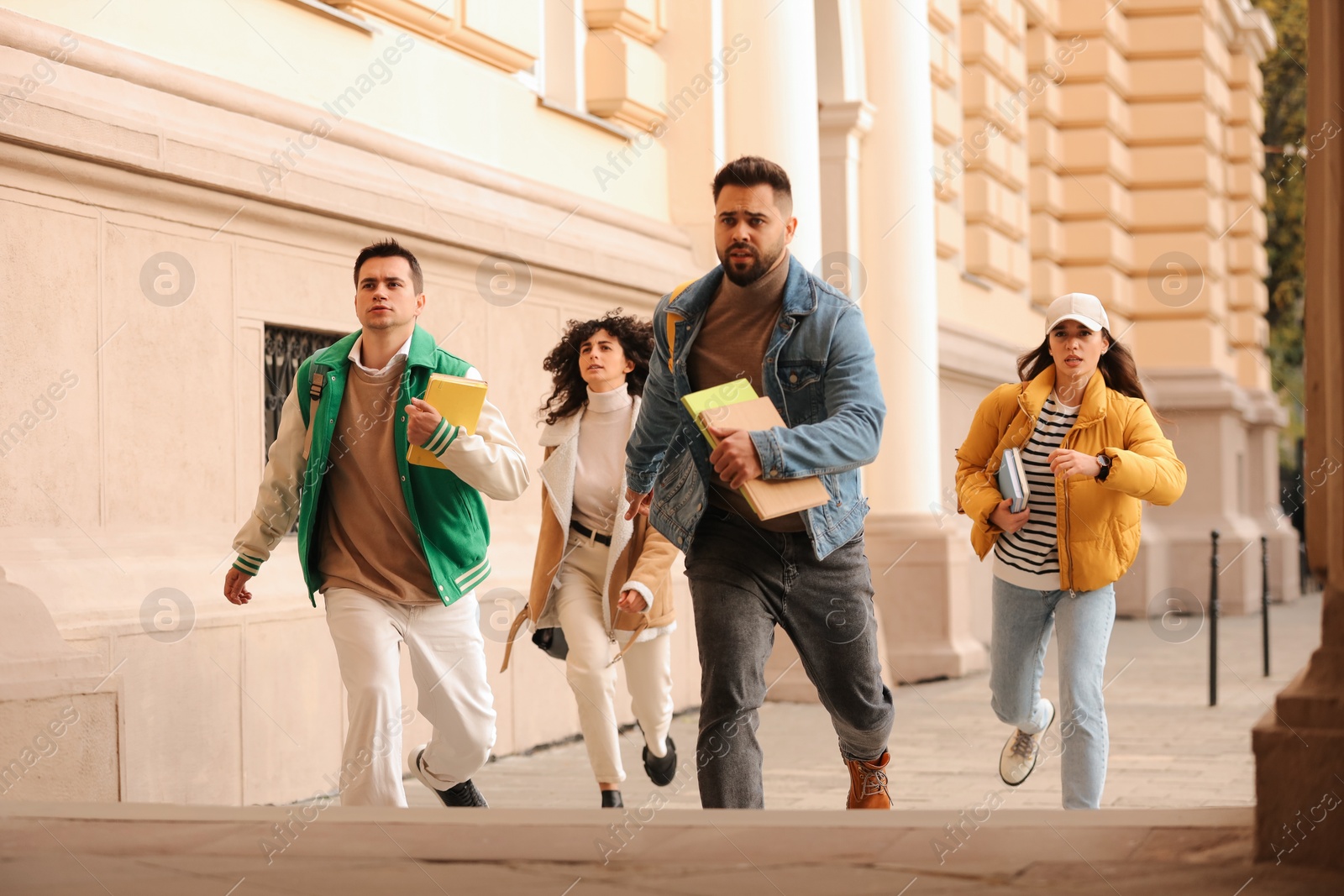 Photo of Being late. Group of students running towards building outdoors