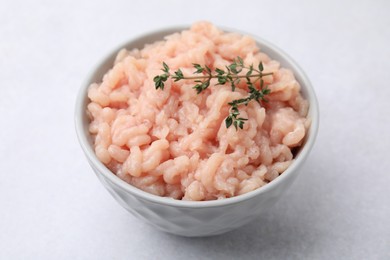 Photo of Fresh raw minced meat and thyme in bowl on light grey table, closeup