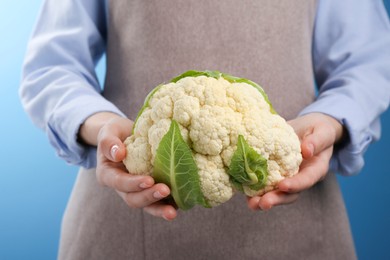 Photo of Woman holding fresh cauliflower against blue background, closeup