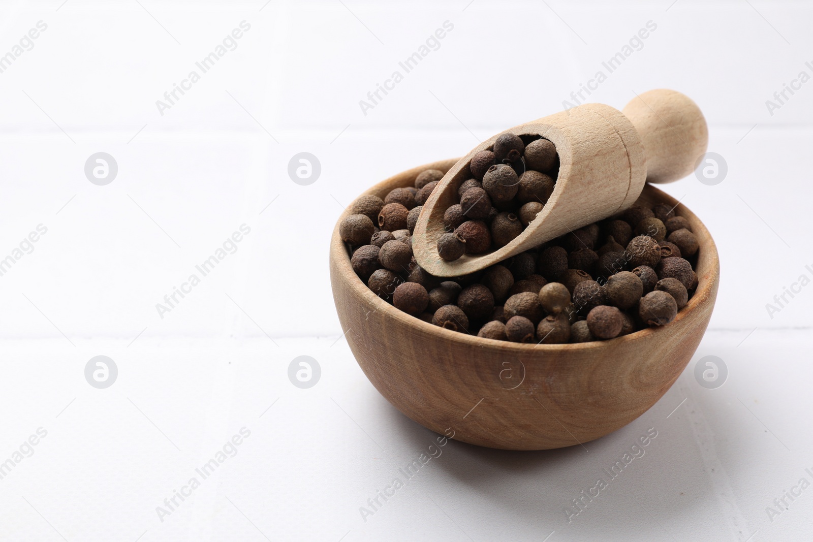 Photo of Dry allspice berries (Jamaica pepper) on white tiled table, space for text