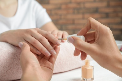 Manicurist applying polish on client's nails at table, closeup. Spa treatment