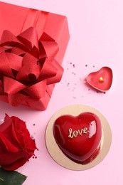 Photo of St. Valentine's Day. Delicious heart shaped cake, gift and rose on light pink background, flat lay