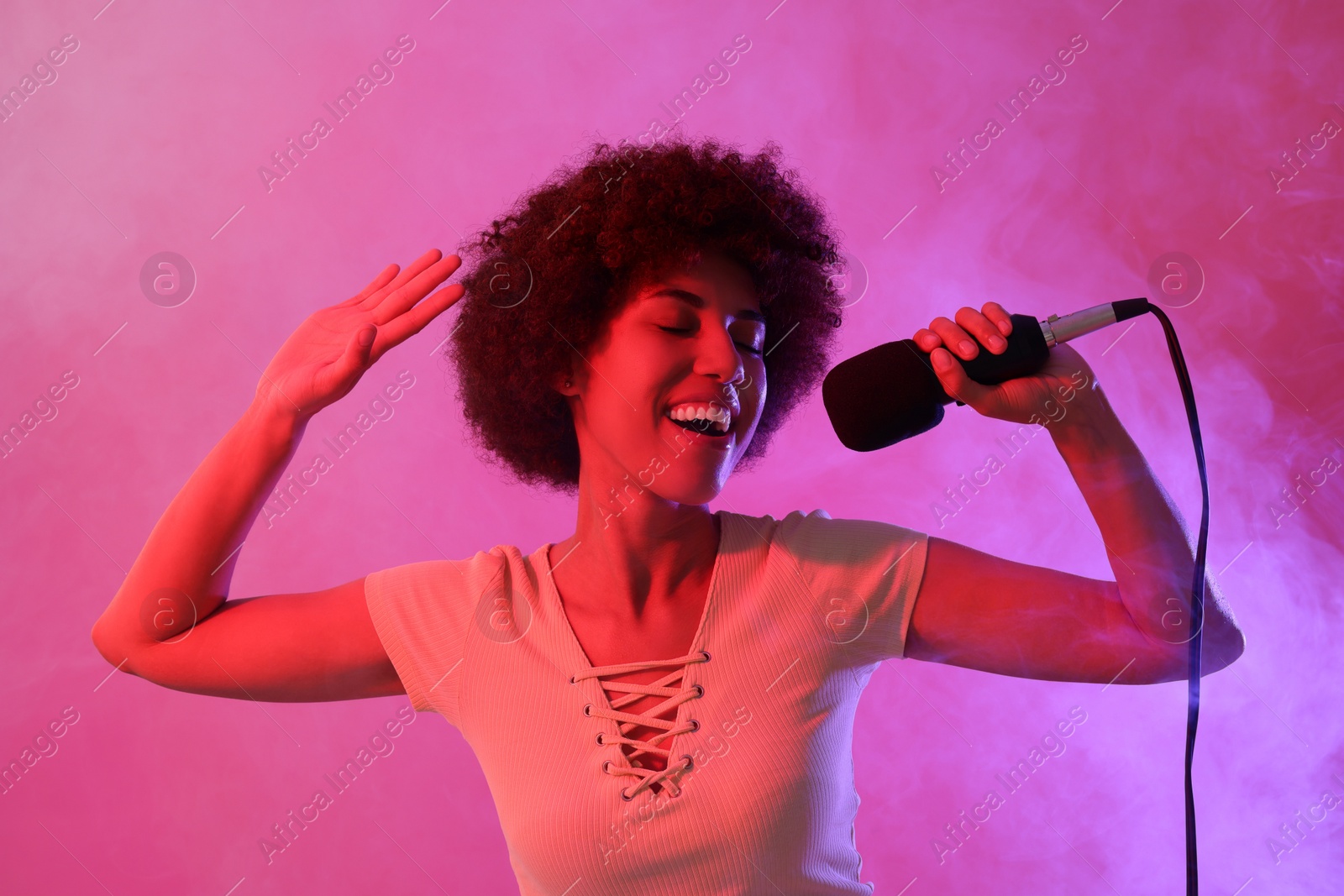 Photo of Curly young woman with microphone singing on pink background. Color tone effect