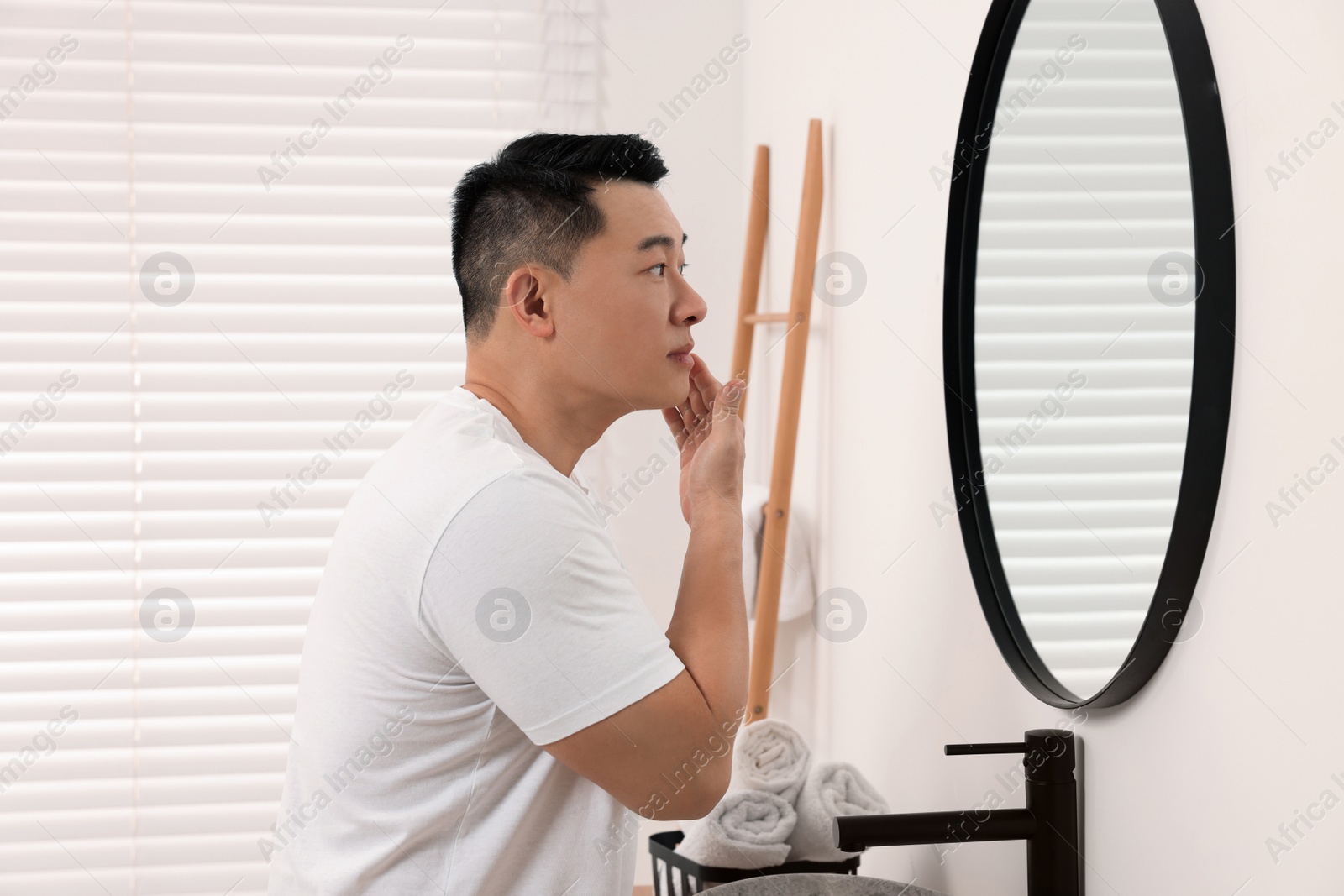 Photo of Handsome man applying cream onto his face near mirror in bathroom