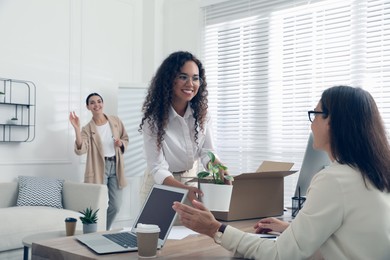 Photo of New employee unpacking box while talking with coworkers in office