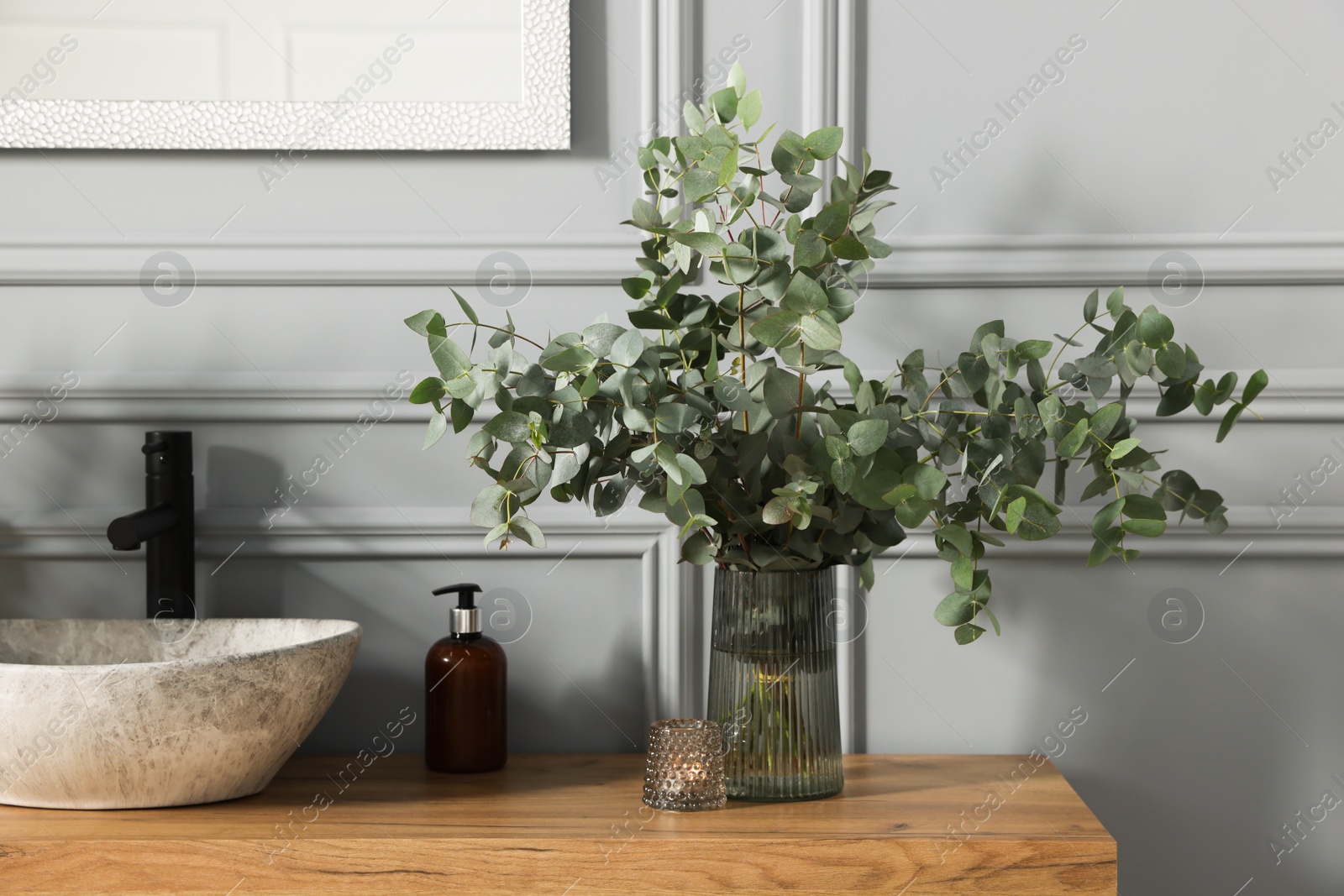 Photo of Eucalyptus branches near vessel sink on bathroom vanity. Interior design