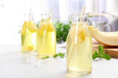 Bottles with tasty melon ball drink on light table