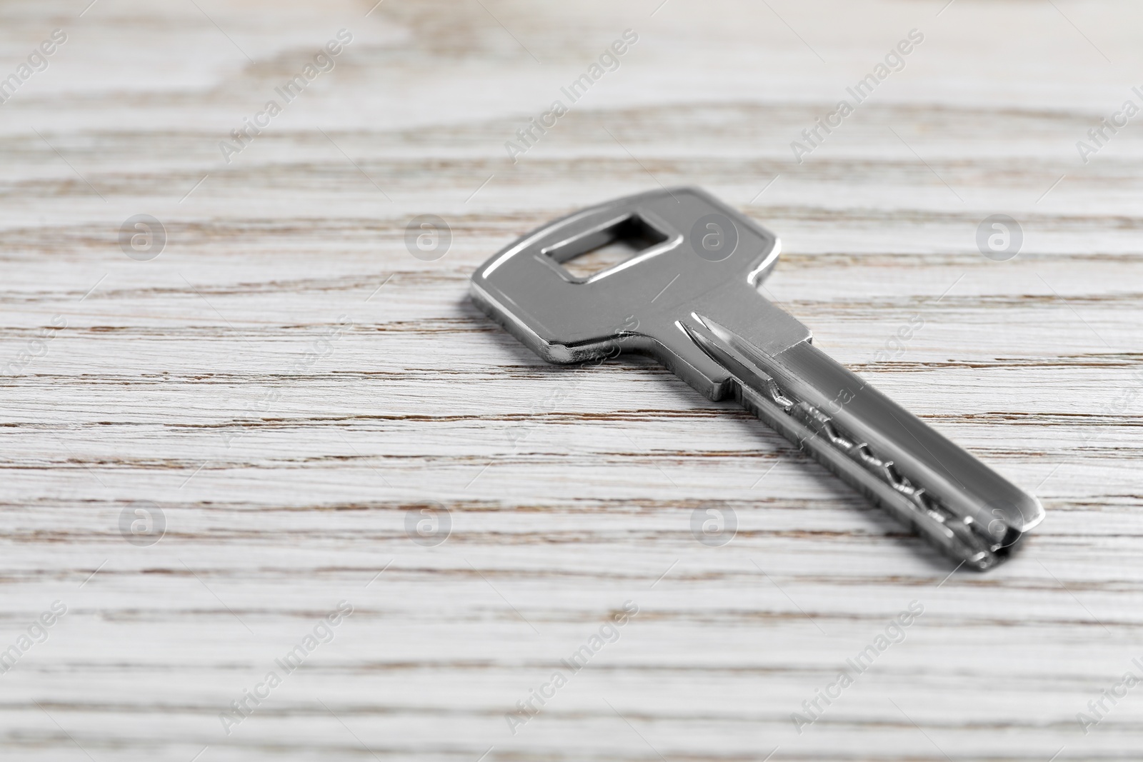 Photo of One key on light wooden table, closeup. Space for text