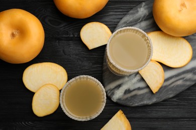 Photo of Glasses of freshly made turnip juice on black wooden table, flat lay