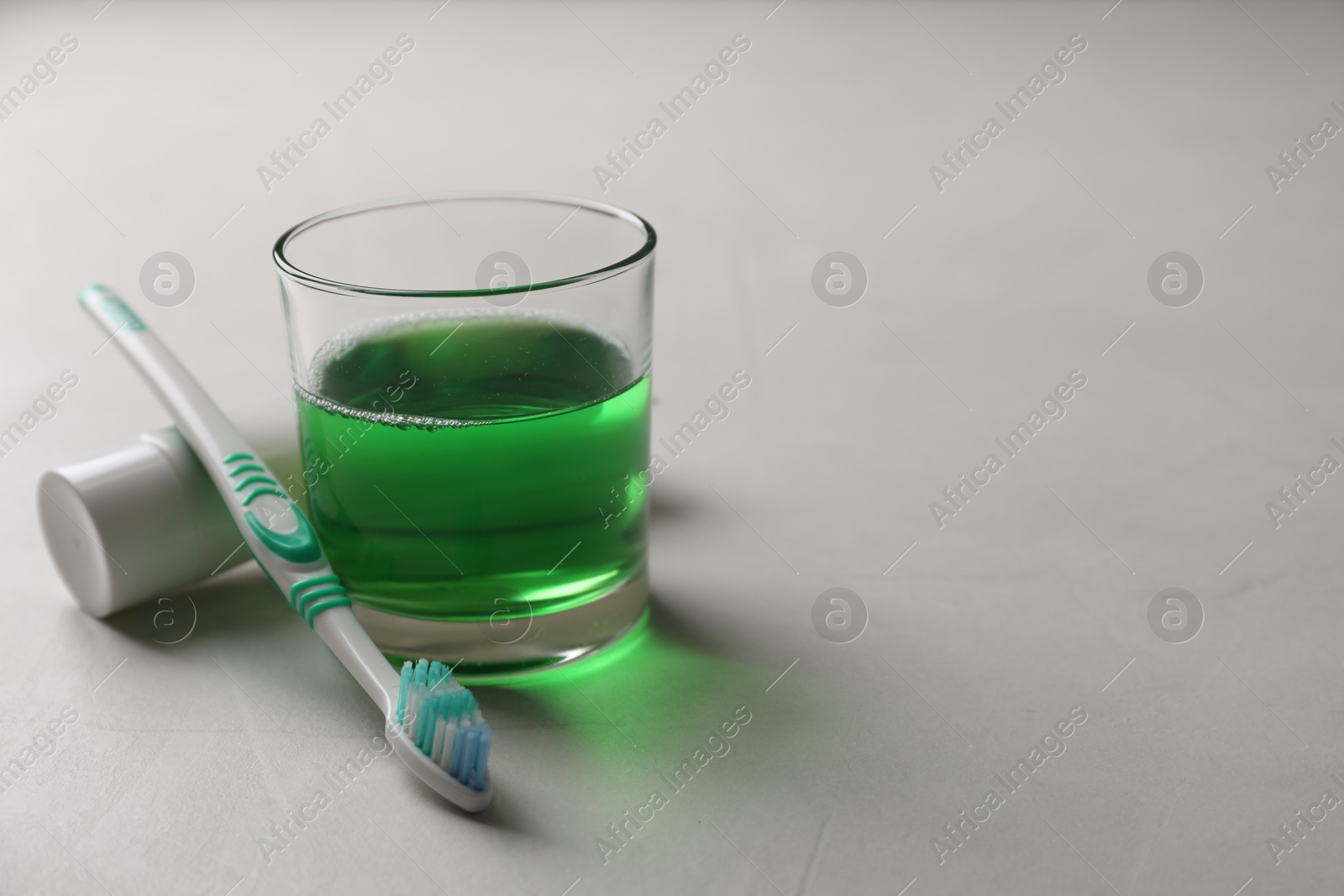 Photo of Fresh mouthwash in glass, toothpaste and toothbrush on light background, closeup. Space for text