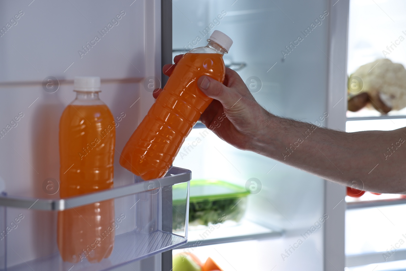 Photo of Man taking bottle of juice out of refrigerator at night, closeup