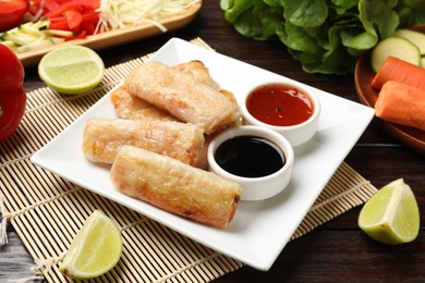 Photo of Tasty fried spring rolls, sauces and fresh products on wooden table, closeup