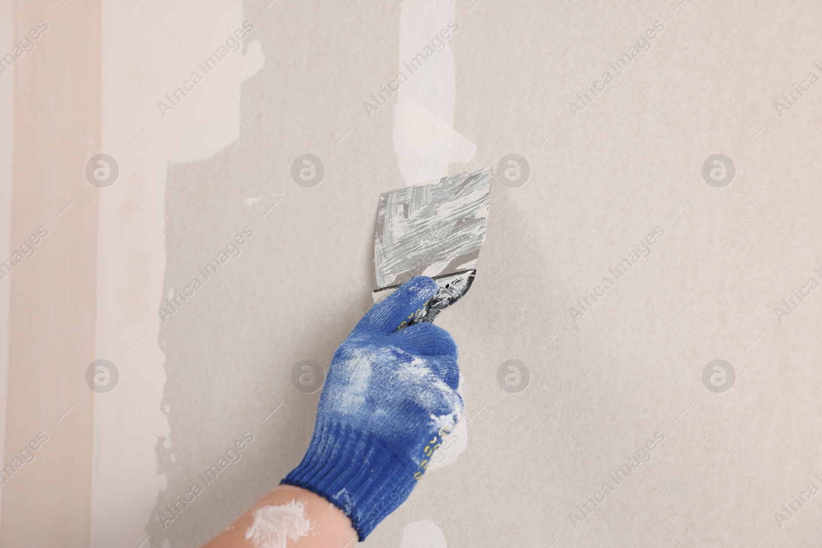 Photo of Man plastering wall with putty knife indoors, closeup. Home renovation