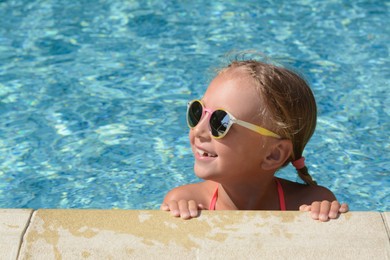 Photo of Happy cute little girl with sunglasses at edge of swimming pool on sunny day. Space for text