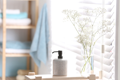 Photo of Soap dispenser and flowers on wooden stand in bathroom